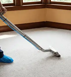 Steam carpet cleaning technician using a hot-water extraction wand on a residential carpet, wearing blue protective shoe covers Aurora, IL.