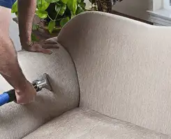 Professional upholstery cleaner deep-cleaning a fabric sofa with a handheld extraction tool and hose in Aurora, IL.